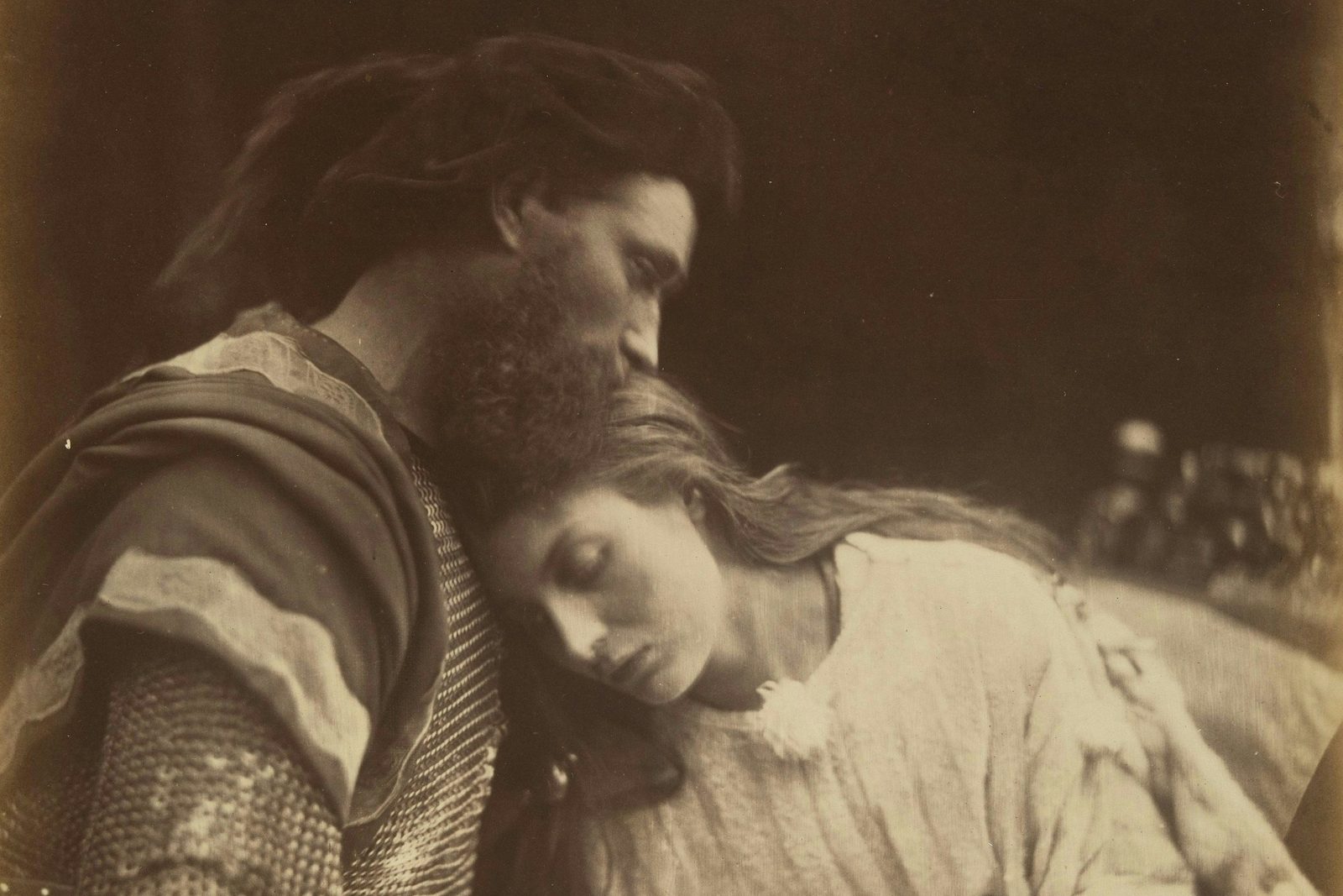 Sepia photograph of a bearded knight in chain mail resting his face against the head of a young woman with long hair, her eyes closed